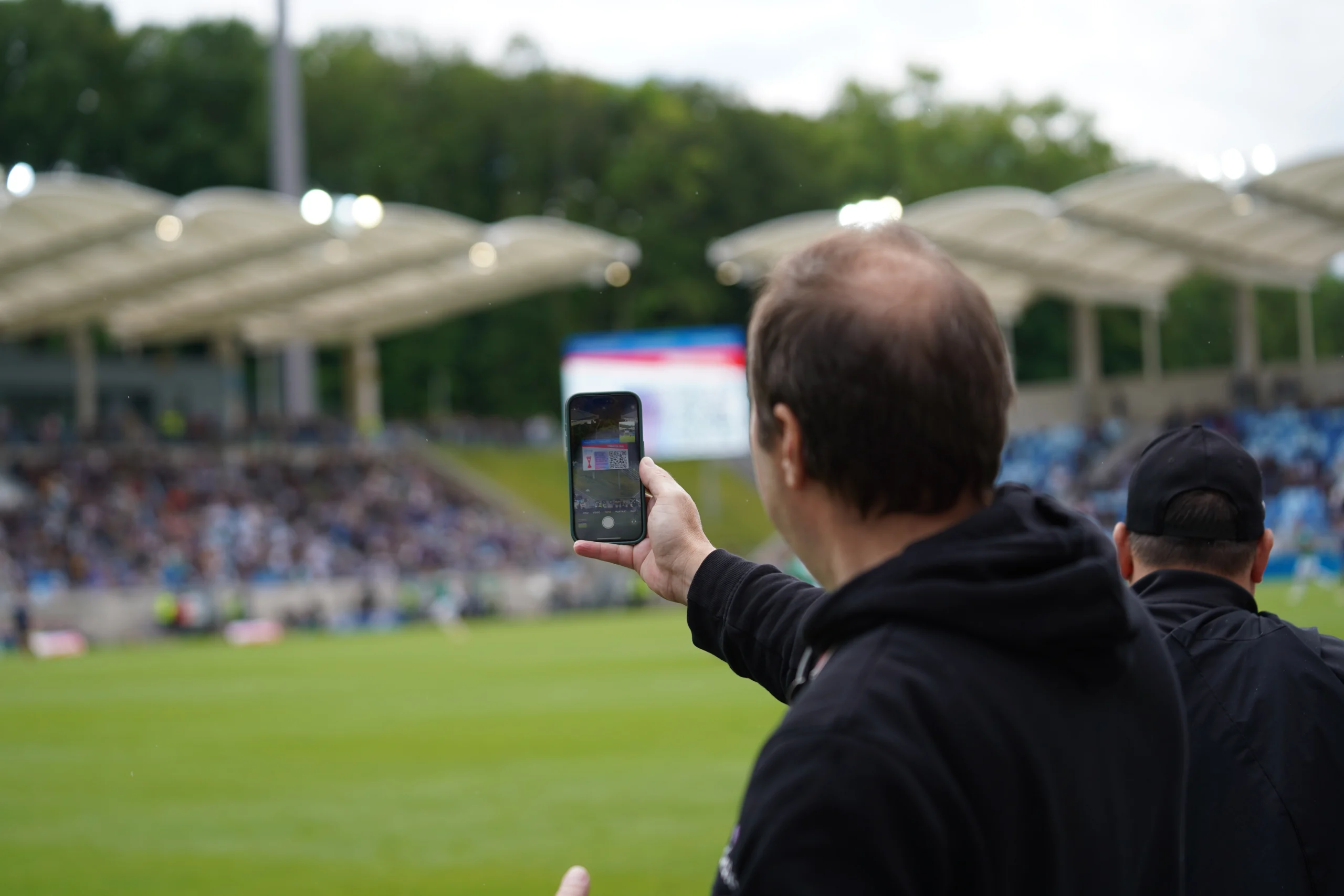 A soccer fan scanning a QR code off a jumbotron